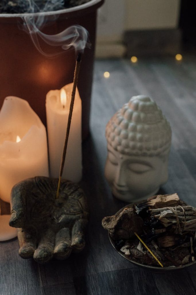 A calming scene with incense and candles beside a Buddha sculpture, embodying tranquility.